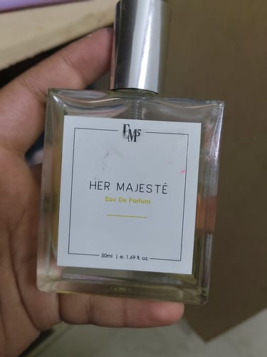 Customer's hand holding a square glass bottle of Her Majesté Eau De Parfum with a silver cap.
