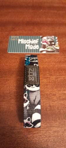 Customer's Mischief Mode bracelet with a raccoon pattern next to its matching display card on a wood table.