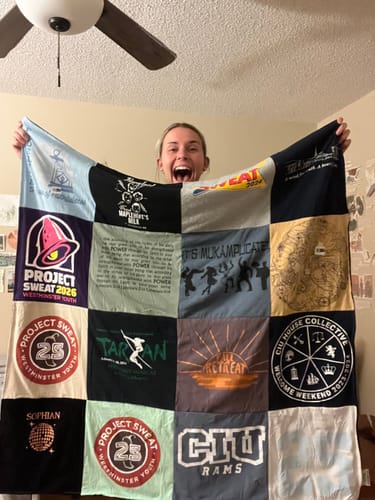 Customer's Project Repat T-Shirt Quilt held up by a smiling person to show the colorful custom patchwork design.