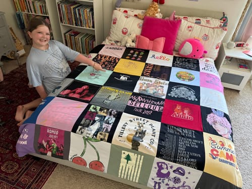 Customer's smiling child pointing to their custom Project Repat T-Shirt Quilt laid out on a bed in a bedroom.