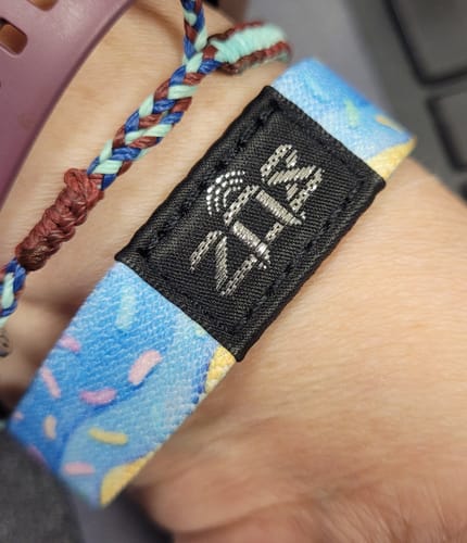 Customer's Happy Birthday bracelet on a wrist, featuring a black ZOX tag with a vibrant blue, pink, and yellow pattern.