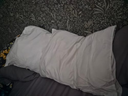 Customer's white Bambutyynyliina pillowcase on a bed with patterned wallpaper in the background.
