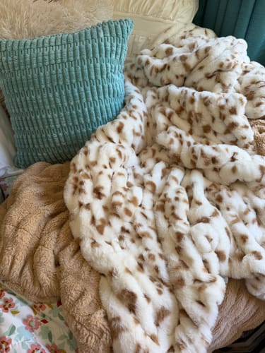 Customer's Hugs Spotted Fawn blanket with cream and tan spotted pattern, sitting next to a textured teal pillow.