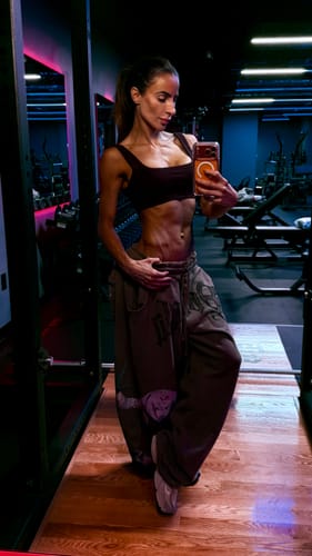 Reviewer in a gym wearing dark baggy Heritage Cargo Sweats and a cropped top, looking into a phone mirror