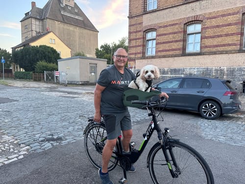 Customer's small white dog sitting comfortably in a dark green Kvisp Dog Bike Carrier mounted on an adult's bicycle.