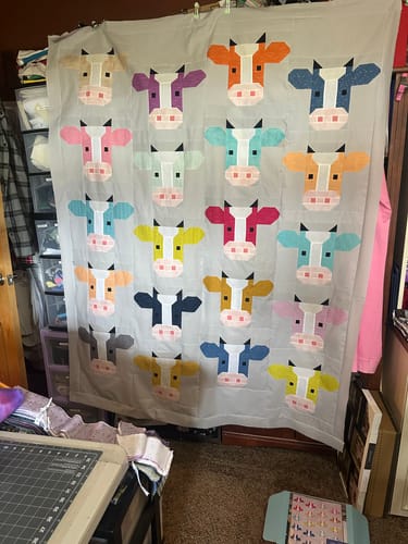 Customer's Annabelle Quilt Kit with completed cow blocks arranged in a grid, hanging against a dark wall.