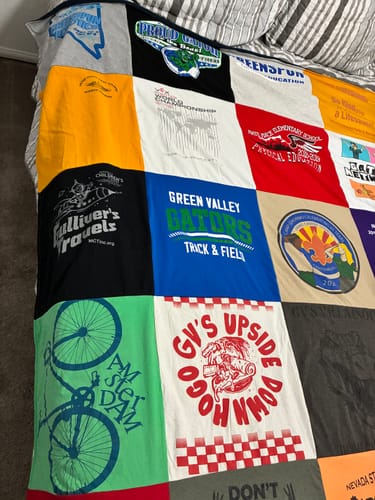 Customer's Project Repat T-Shirt Quilt featuring various colorful, patterned shirt panels on a bed.