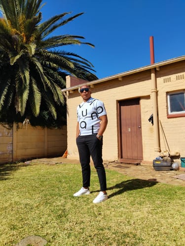 Reviewer standing outdoors wearing a white knit top with black letters, black pants, and white sneakers.