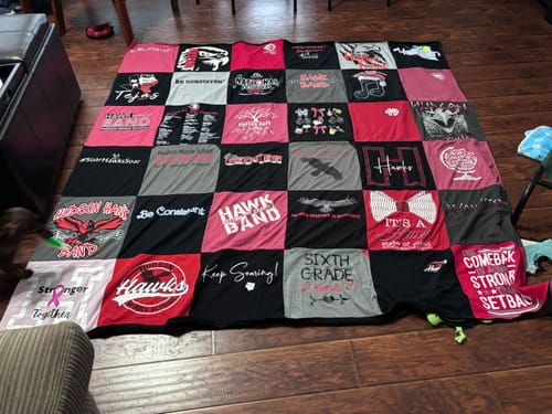 Customer's Project Repat T-Shirt Quilt featuring a grid of red, pink, grey, and black shirts on a wooden floor.