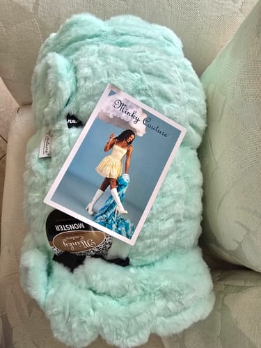 Customer's Hugs Light Aqua Serene Blanket with promotional tag attached, resting on a textured surface.
