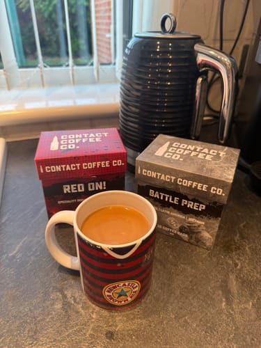 Reviewer's Battle Prep and Red On coffee bags next to a mug of coffee and a black kettle on a kitchen counter.