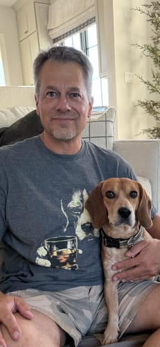 Customer's Whiskey Beagle Grunge T-Shirt in grey, worn while holding a pet beagle.