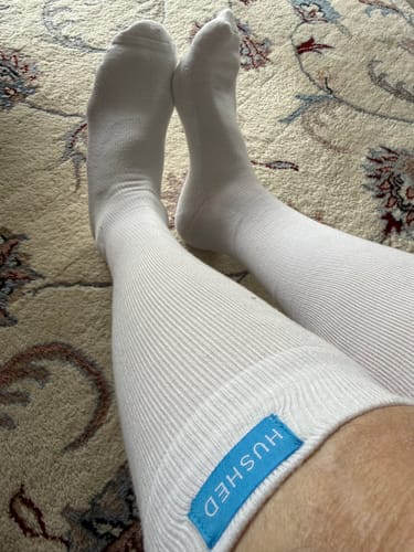Customer's white Hushed compression socks worn on legs, featuring a visible blue Hushed brand tag.