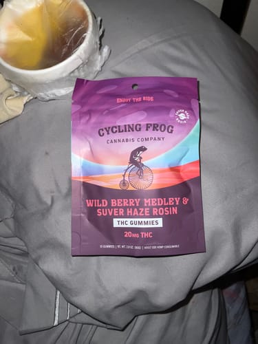 Customer's Wild Berry Medley Rosin Gummies pouch resting on a gray, wrinkled surface near a cup.