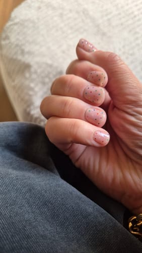 Reviewer's hand wearing Sugar Confetti UV Gel nail wraps with colorful dots on a light pink base.