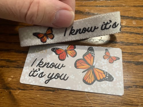 Customer's I Know It's You bracelet held over its matching butterfly-themed display card on a wooden surface.