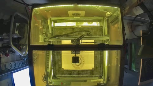 Reviewer's AtomStack A40 Pro V2 laser engraver inside a protective enclosure, showing a glowing workspace.