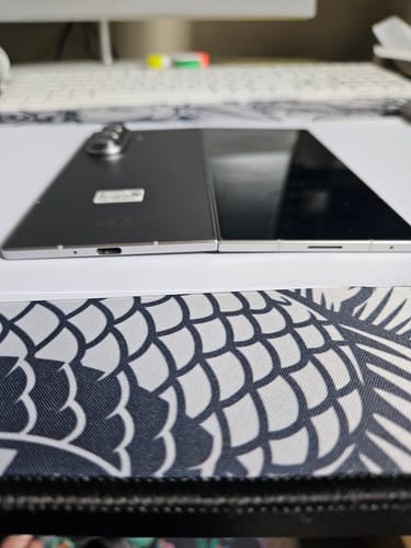 Customer's Samsung Galaxy Z Fold7 lying flat on a patterned surface, side view showing a thin profile.