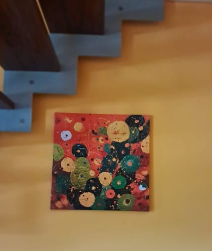 Customer's Fichi di Fuoco painting with colorful circular shapes hanging on a warm yellow wall.