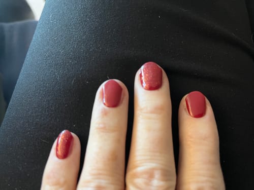 Kundenfoto des UV Top Coat Pink Pearl auf Fingernägeln, die ein glänzendes, rötliches Finish zeigen.