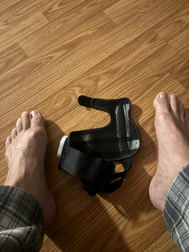 Customer's black Nexalign Pro EMS Bunion Corrector resting on a wooden floor near bare feet.