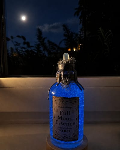 Customer's leuchtende Full Moon Essence Zaubertrank Flasche bei Nacht vor einem Fenster mit Vollmond.