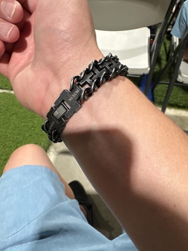 Customer's Connected At The Cross bracelet, made of dark metal, worn on a person's wrist.