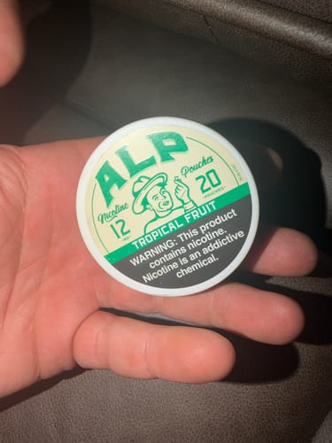 Customer's hand holding a round Tropical Fruit ALP nicotine pouch container.