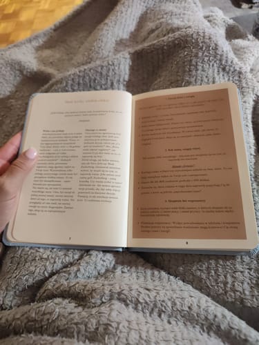 Reviewer's open planner with visible text and motivational quotes, held by a hand over a fuzzy grey blanket.
