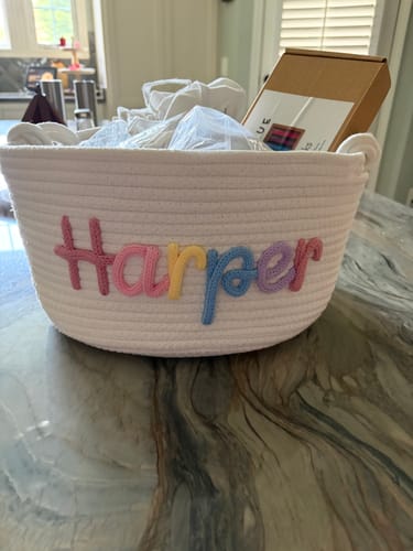 Customer's white Baby Knits personalized knitted basket with the name Harper in colorful yarn, sitting on a counter.
