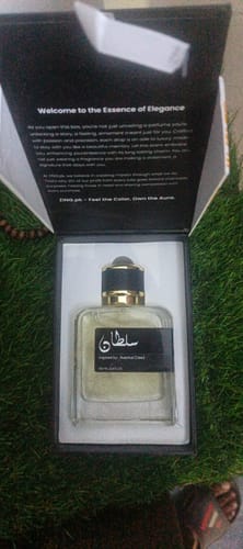 Customer's Sultan perfume bottle in an open, elegant black box resting on a green, grassy surface.