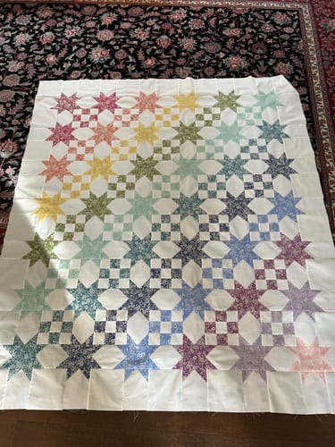 Customer's Star Studded quilt top laid flat on a dark patterned rug, showing colorful star blocks in a gradient layout.