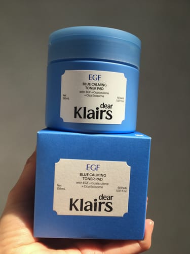 Reviewer's hand holding the blue EGF Blue Calming Toner Pad tub and its matching blue outer box.