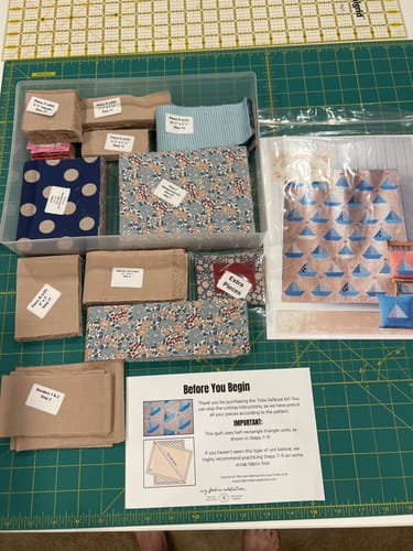 Customer's Tilda Sailboat quilt kit pieces, labeled fabric stacks, and instruction sheet in a clear organizer box.