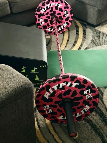 Customer's RitFit pink leopard print bumper plates attached to a barbell, sitting on a gym mat in a home setting.