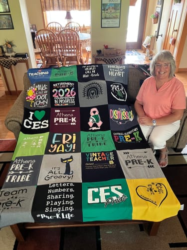 Customer's Project Repat T-Shirt Quilt draped over a couch next to the smiling reviewer.