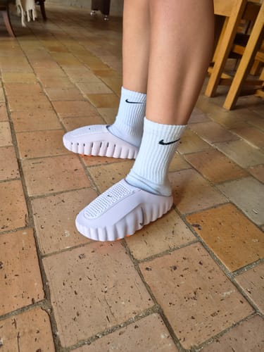 Customer's feet wearing pink Nike Mind 001 slides with white Nike socks, standing on tiled floor.