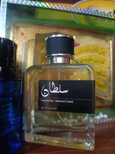 Customer's Sultan perfume bottle with a black cap, standing beside a blue bottle on a wooden surface.