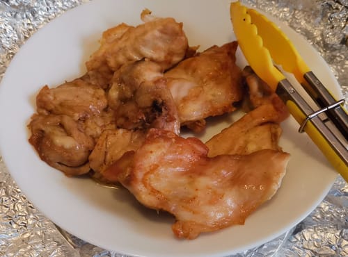 Customer's cooked chicken pieces on a white plate with yellow kitchen tongs