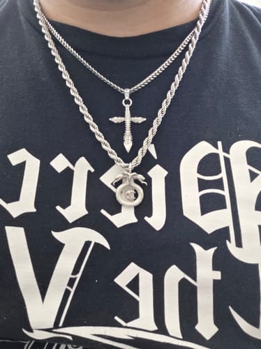Customer's Cuban Chain necklaces layered with a cross pendant and a circular snake pendant against a dark printed shirt.
