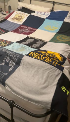 Customer's Project Repat T-Shirt Quilt spread out on a bed, showing various colorful, patterned T-shirt panels.