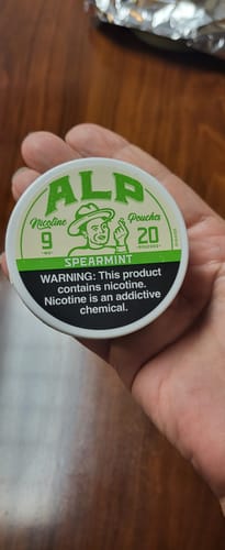 Reviewer's hand holding a round white Spearmint Nicotine Pouches container with a green logo.