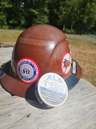 Customer's round tin of Chilled Mint Nicotine Pouches resting on a brown hard hat with stickers.