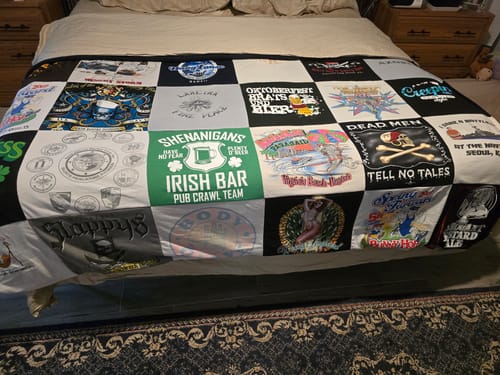 Customer's Project Repat T-Shirt Quilt featuring various colorful graphic t-shirt panels spread out on a made bed.