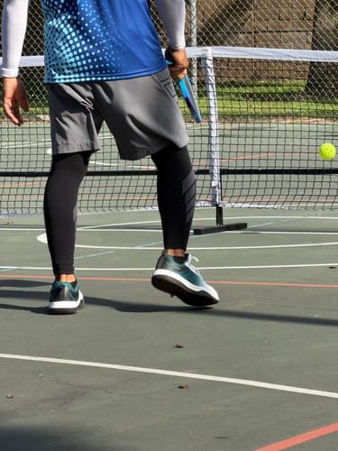 Customer's white and dark green CUURT Muuv court shoes worn while playing pickleball on an outdoor court.
