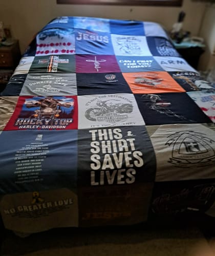 Customer's Project Repat T-Shirt Quilt draped over a bed, showing various custom graphics and t-shirt fabrics.