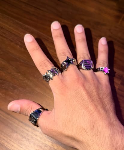 Customer's hand wearing five different silver metal rings with star and geometric designs.