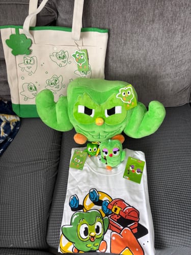 Customer's Duolingo x MINISO Duo plush charm and branded merchandise, including a tote bag and t-shirt.
