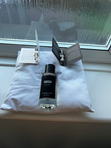 Customer's Smoke & Mirrors Eau de Parfum bottle and complimentary samples on a white cloth, by a window.