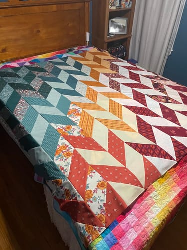 Customer's completed Herringbone Ombre Quilt on a wooden bed frame, showing the colorful desert-toned pattern.